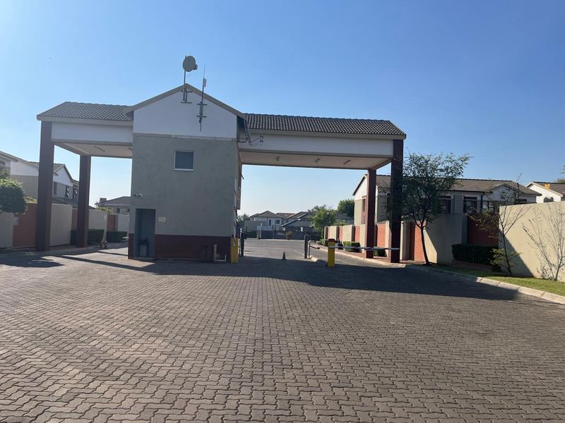 A view of the secure gated entrance and guardhouse for the townhouse complex, featuring paved driveway access and perimeter walling.