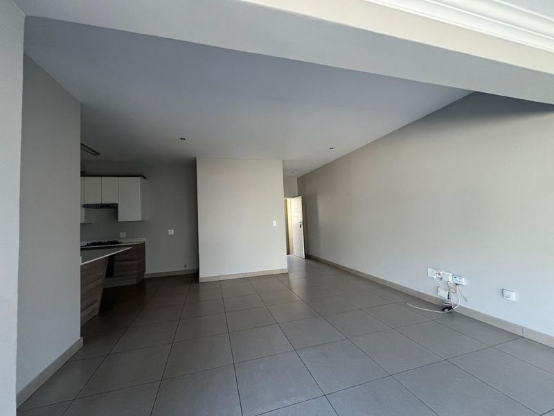 An open-plan living and kitchen area featuring neutral tiled flooring, modern cabinetry, and recessed lighting in a clean, vacant space.