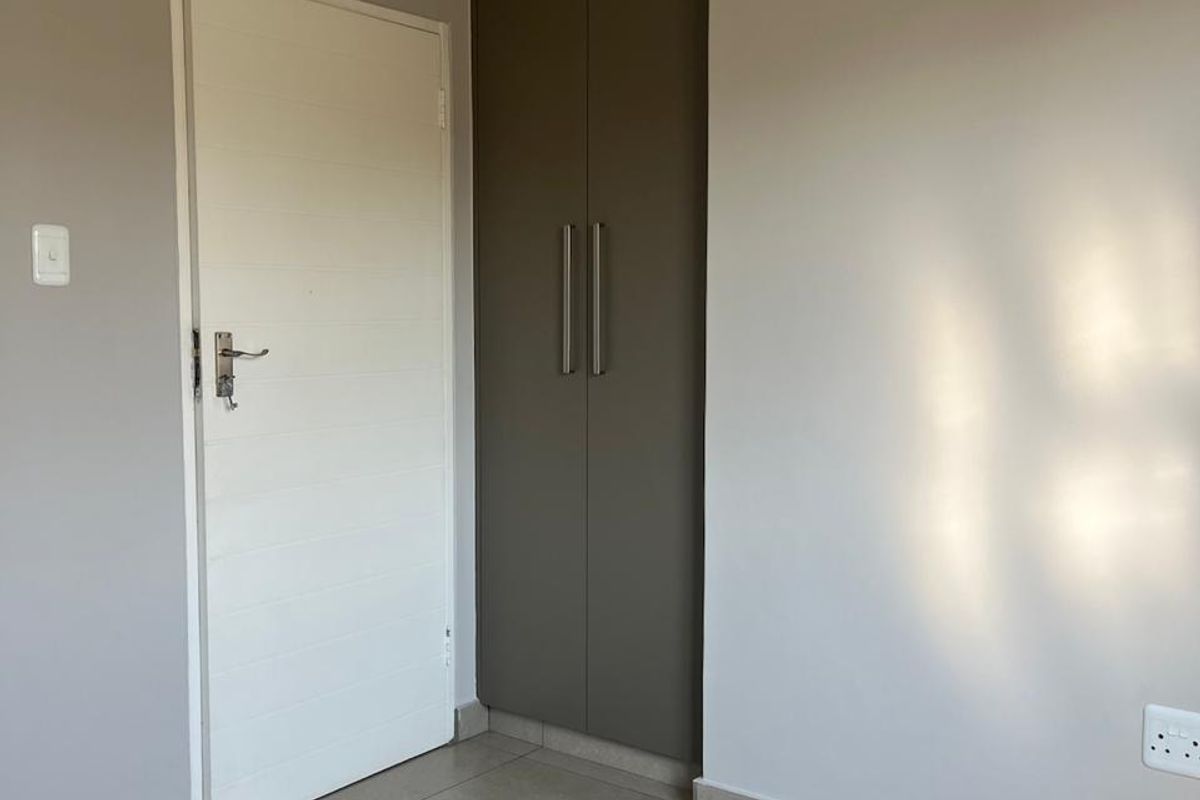 A clean, empty bedroom featuring neutral wall tones, modern floor tiles, and a tall built-in cupboard with sleek hardware.