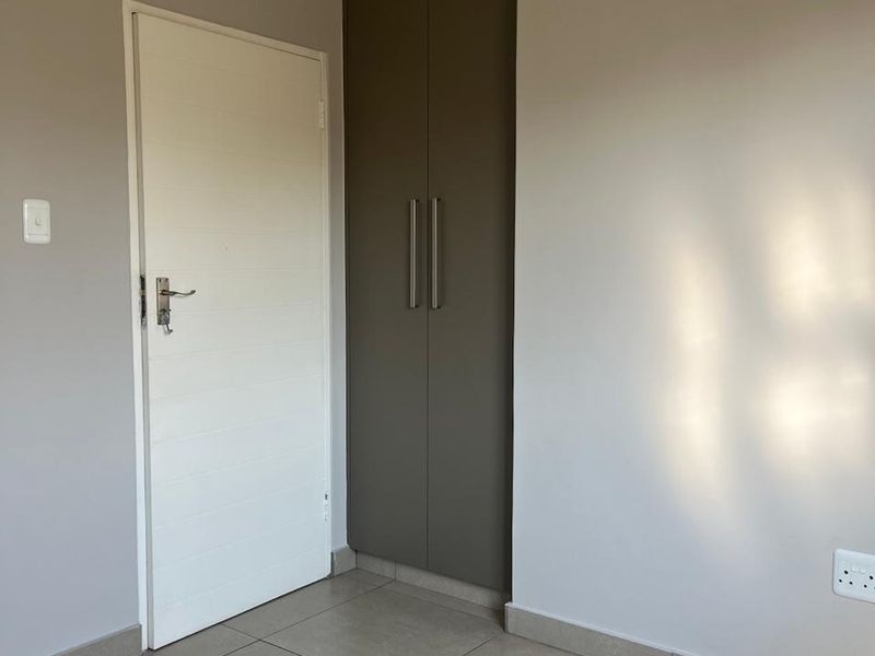 A clean, empty bedroom featuring neutral wall tones, modern floor tiles, and a tall built-in cupboard with sleek hardware.