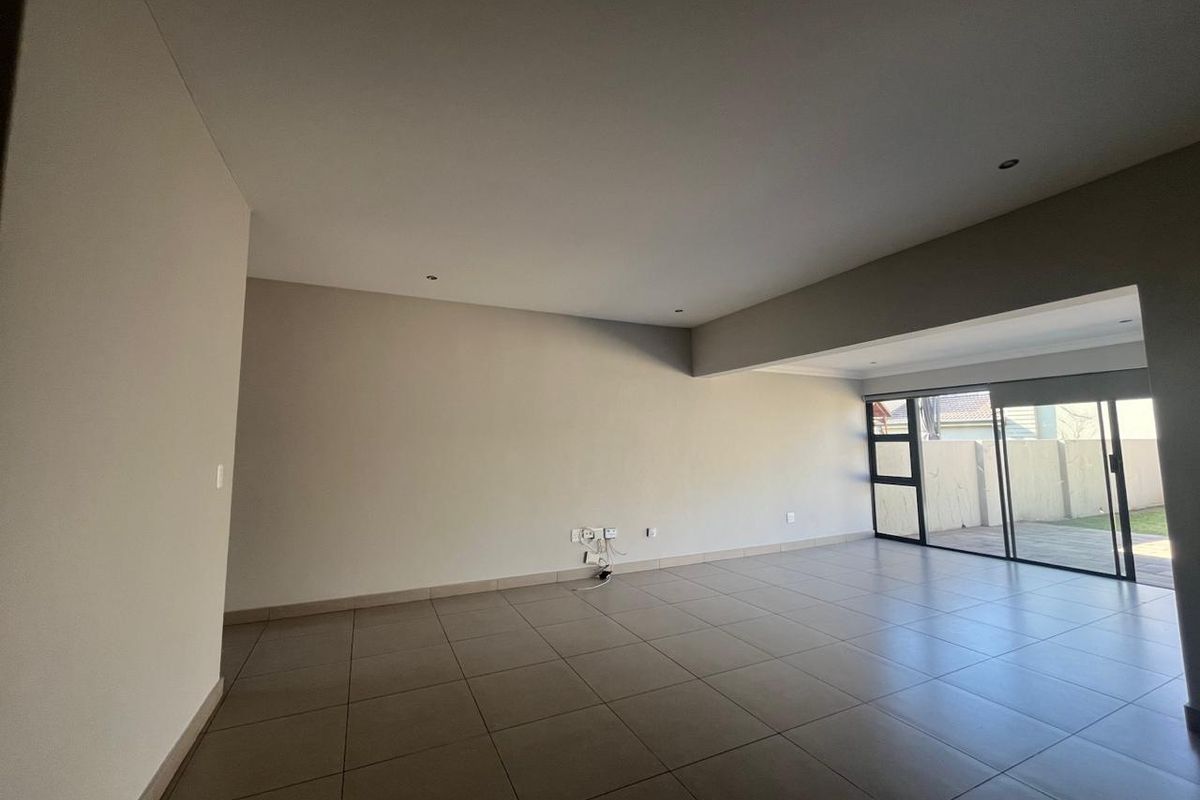 Spacious, empty living area featuring neutral tiled flooring, recessed lighting, and large sliding glass doors providing access to the outdoor space.