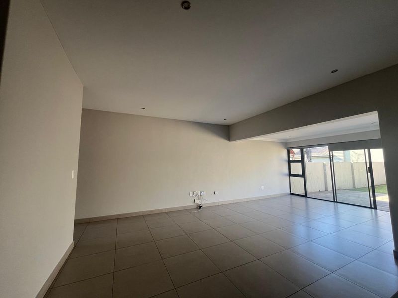 Spacious, empty living area featuring neutral tiled flooring, recessed lighting, and large sliding glass doors providing access to the outdoor space.