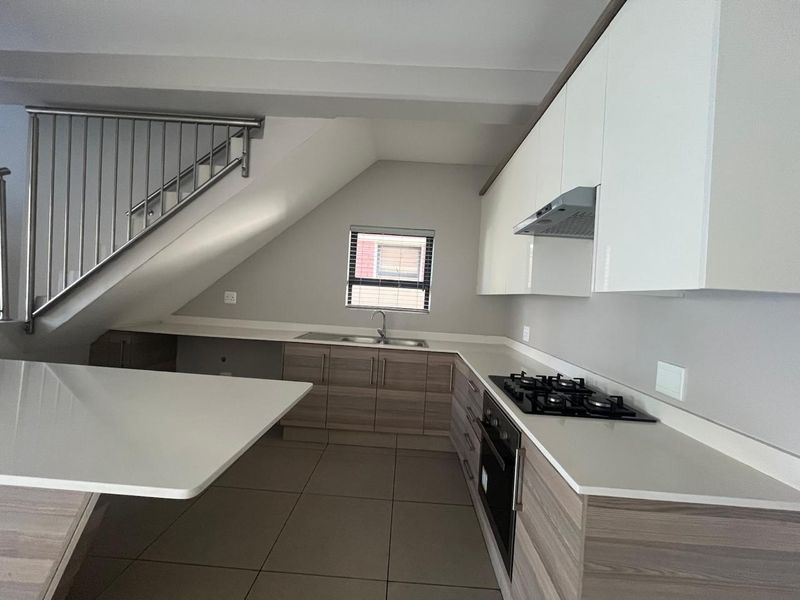 Modern kitchen featuring sleek cabinetry, stone countertops, integrated gas hob, oven, and extractor fan, situated beneath a staircase with a metal balustrade.