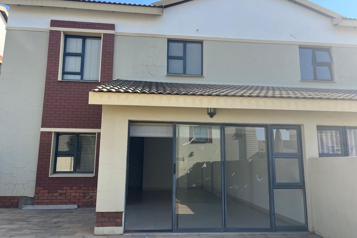 Rear view of the townhouse featuring a paved patio area, sliding glass doors, and a combination of brick and plastered exterior finishes.