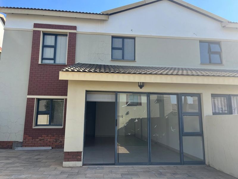 Rear view of the townhouse featuring a paved patio area, sliding glass doors, and a combination of brick and plastered exterior finishes.