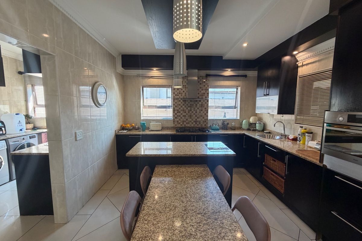 Modern kitchen featuring dark cabinetry, granite countertops, a central island with integrated dining space, gas hob, and tiled finishes throughout.