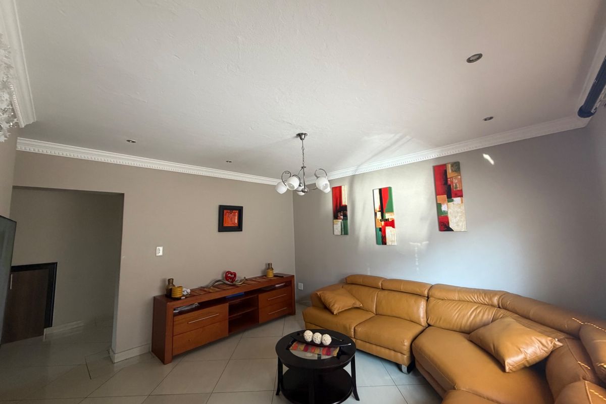 A well-maintained living room featuring tiled flooring, decorative ceiling cornicing, and recessed downlighting.
