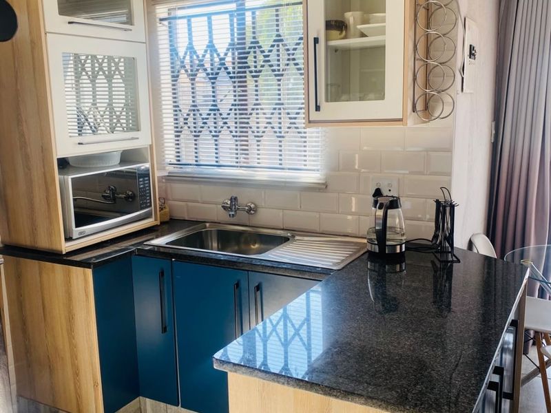 A modern, compact kitchen featuring blue and wood-tone cabinetry, granite countertops, subway tile backsplash, and a built-in microwave.