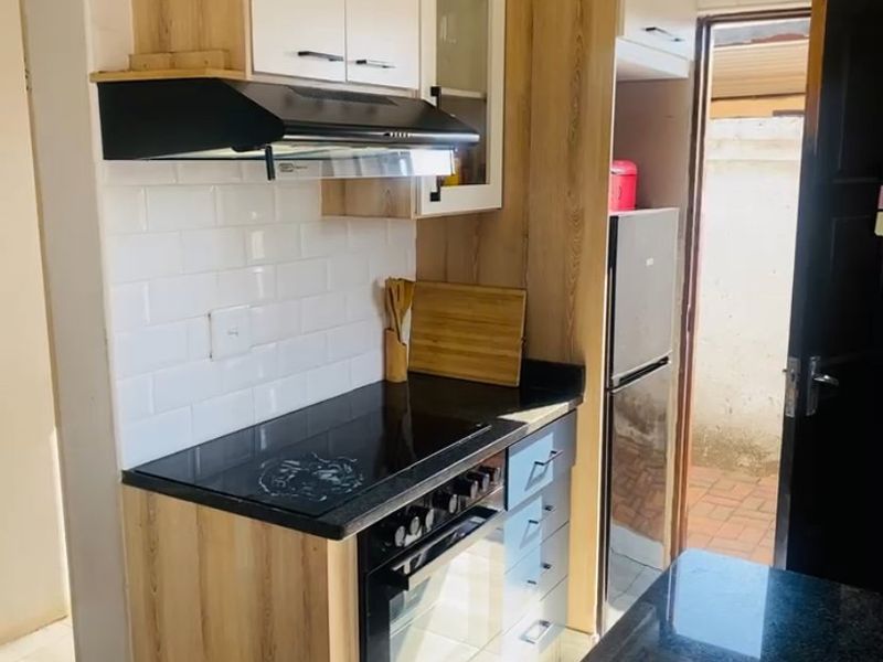 A compact, modern kitchen featuring light wood-tone cabinetry, granite countertops, a subway tile backsplash, and integrated cooking appliances.