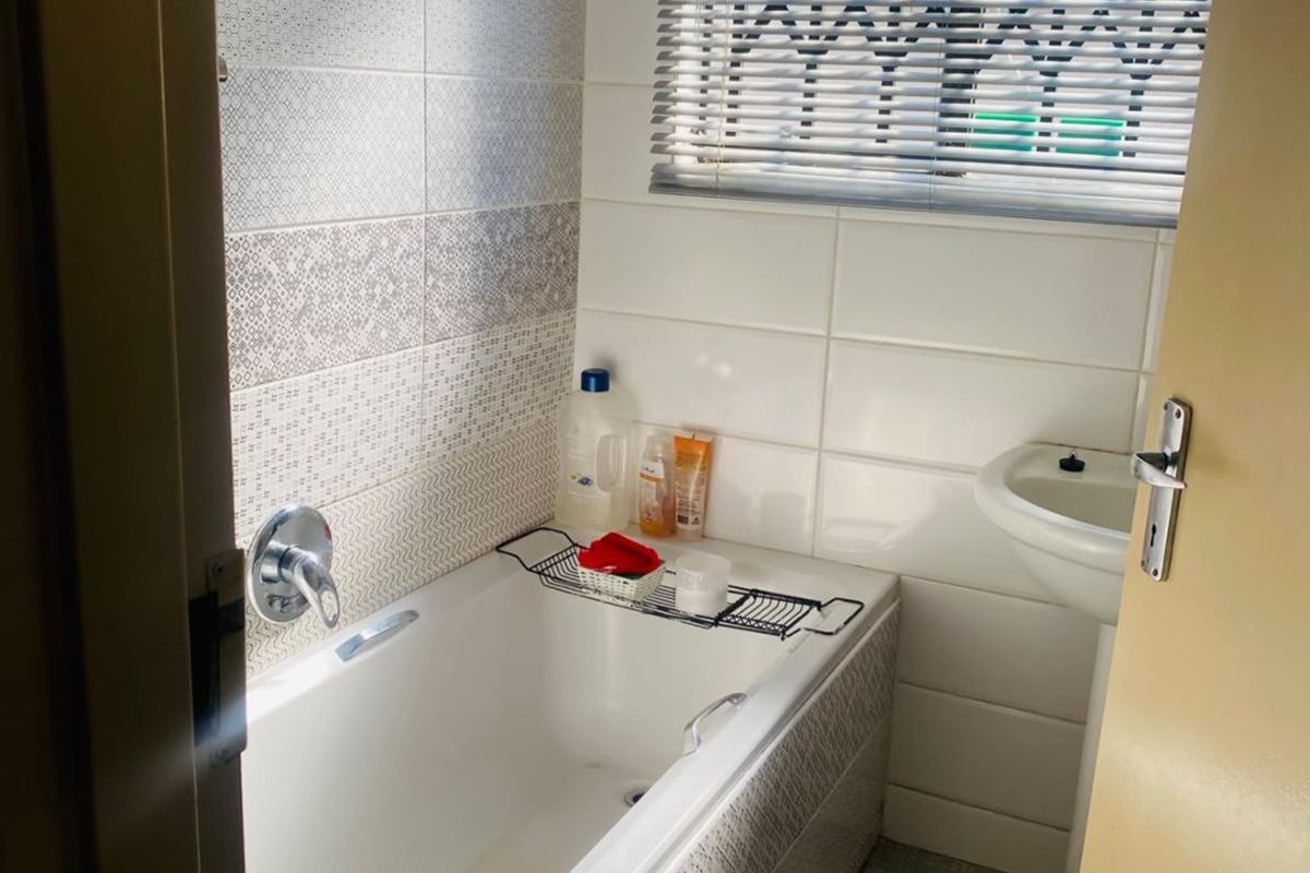 A compact bathroom featuring a bathtub, pedestal basin, and neutral tiled finishes, providing a functional space with natural light.