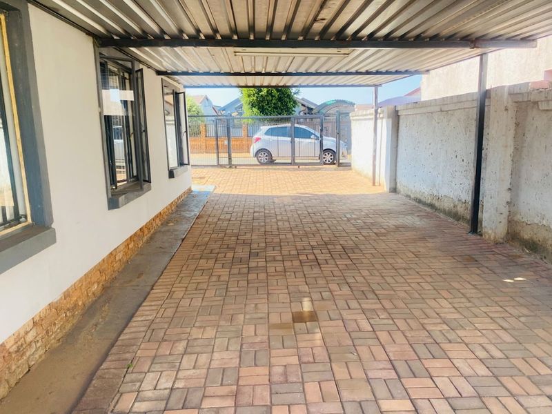 A covered carport area featuring paved flooring, a corrugated metal roof, and a secure gated entrance.