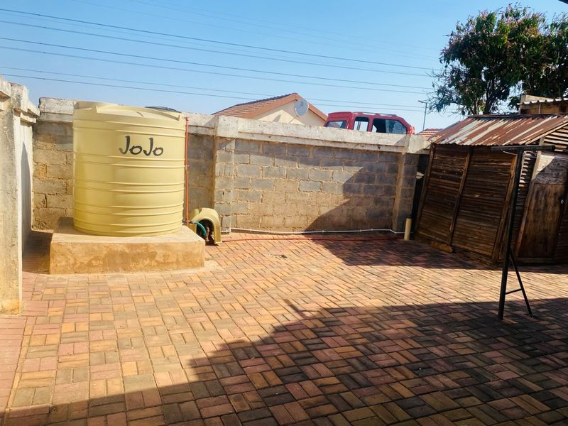 Rear courtyard area featuring a paved surface, a water storage tank, and a small storage shed with a corrugated metal roof.