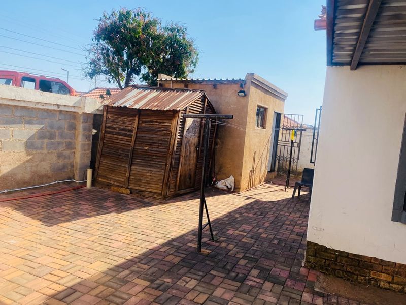 Rear courtyard area featuring paved flooring, a wooden storage shed, an outbuilding, and a rotary clothesline within a walled perimeter.