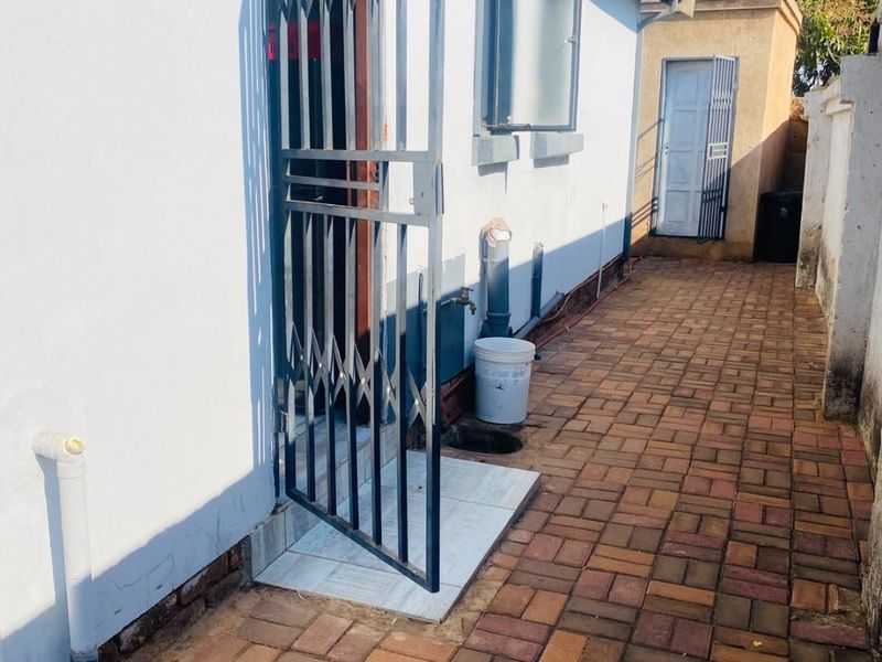 A side exterior walkway featuring paved flooring, a security gate, and an external water tap along the side of the house.