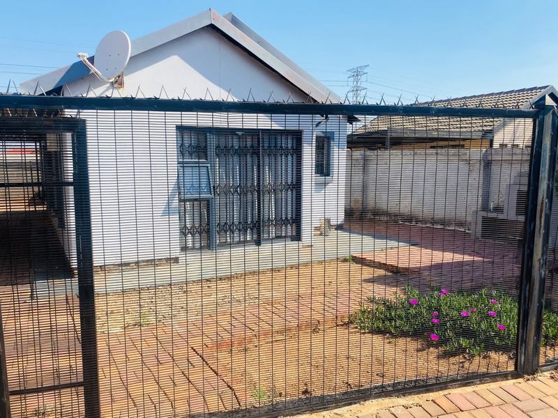 Rear exterior view of the property featuring a paved patio area, security fencing, and basic garden landscaping.