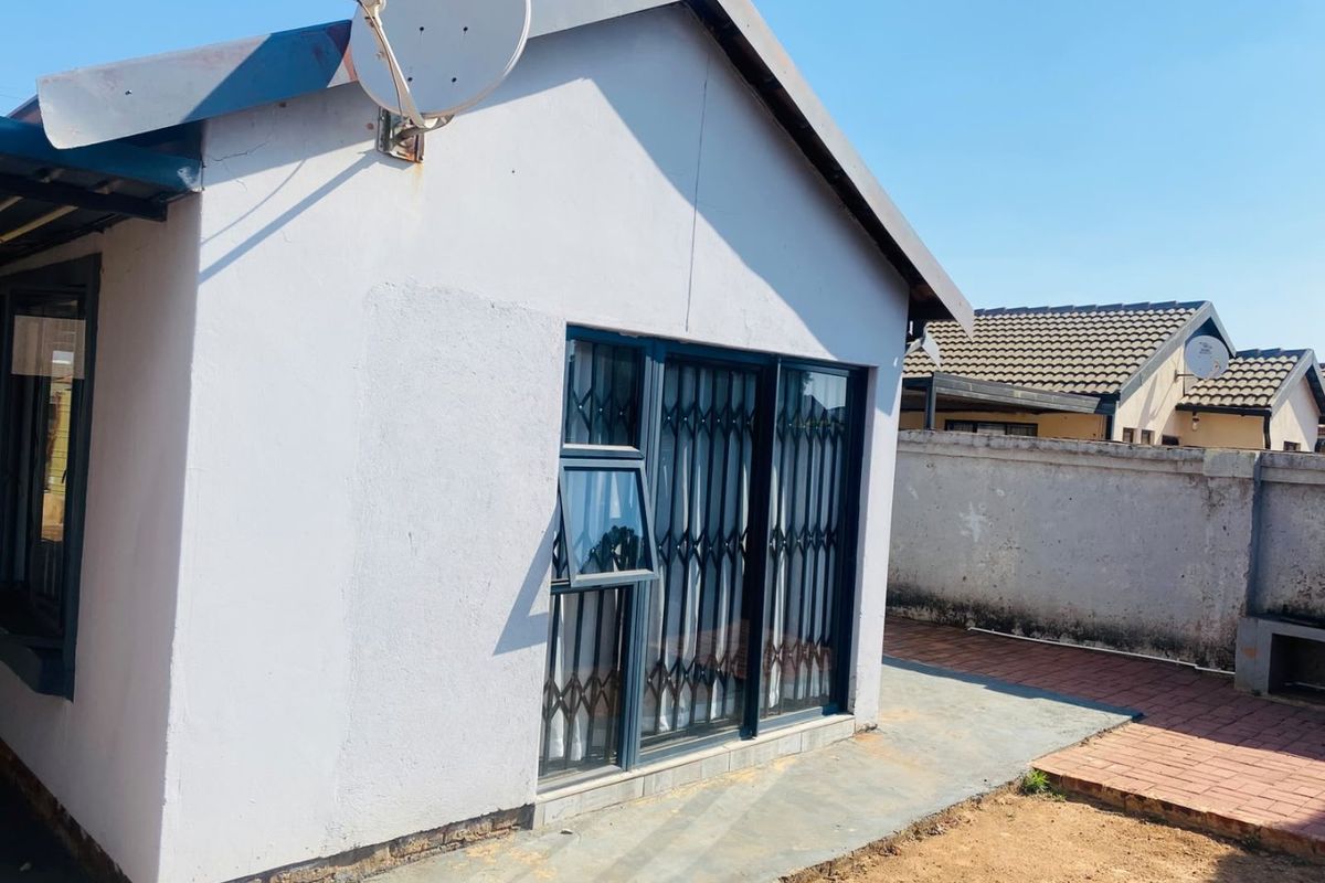 Rear view of the property featuring a sliding glass door with security gate, satellite dish, and paved walkway along the boundary wall.