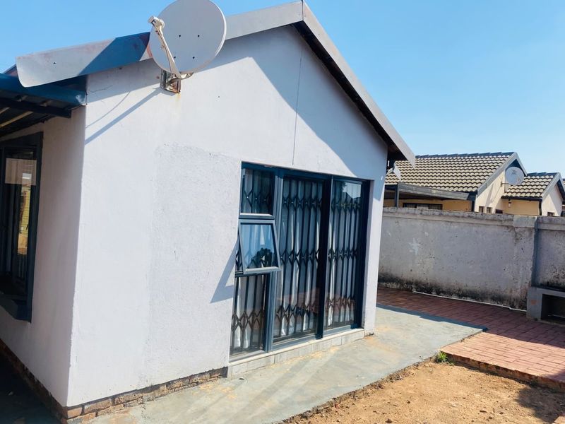 Rear view of the property featuring a sliding glass door with security gate, satellite dish, and paved walkway along the boundary wall.