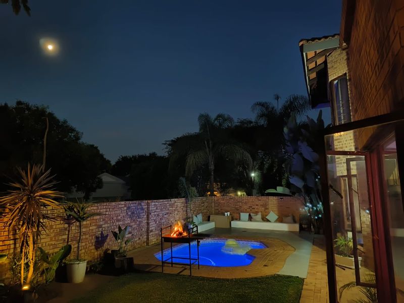 Night view of a backyard pool area featuring a paved surround, built-in bench seating, and a brick boundary wall.