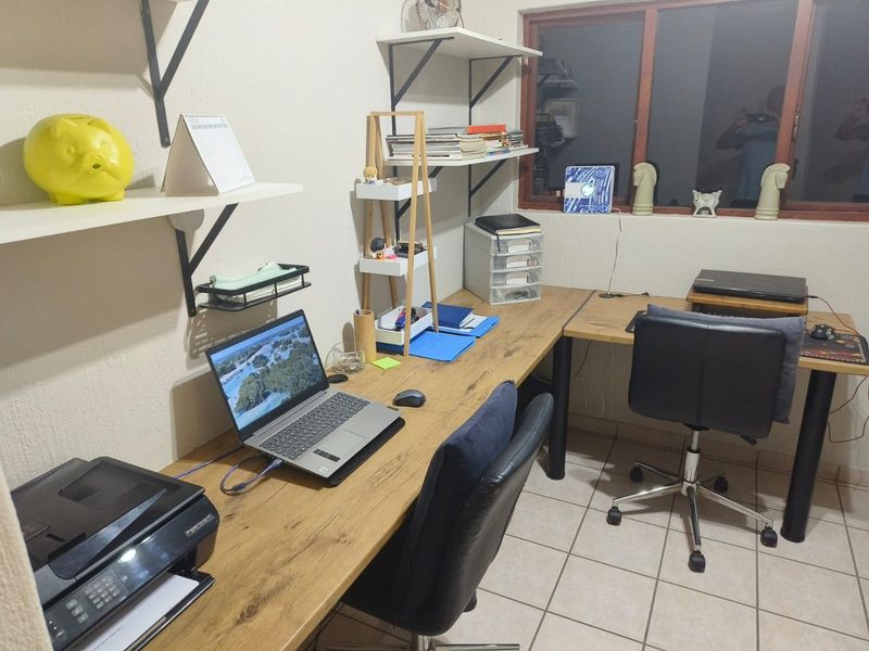 A functional home office space featuring tiled flooring, built-in wall shelving, and a timber-framed window.