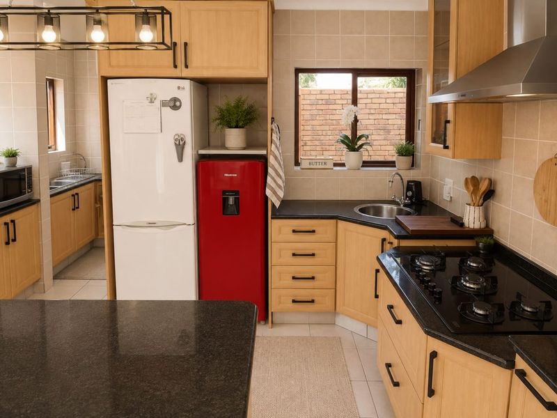 Well-appointed kitchen featuring light wood cabinetry, dark granite countertops, a gas hob with extractor, and a functional layout with an adjacent scullery area.