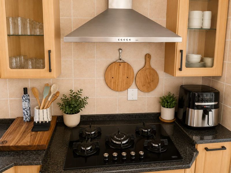 A well-maintained kitchen area featuring a modern gas hob, stainless steel extractor fan, granite countertops, and ample built-in wooden cabinetry.
