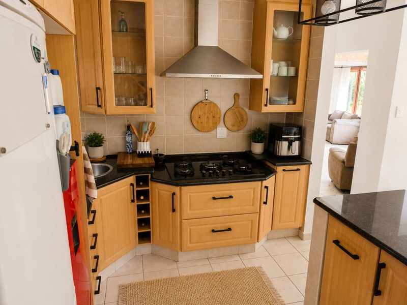 A functional kitchen featuring light wood cabinetry, granite countertops, a gas hob with a stainless steel extractor fan, and tiled flooring.