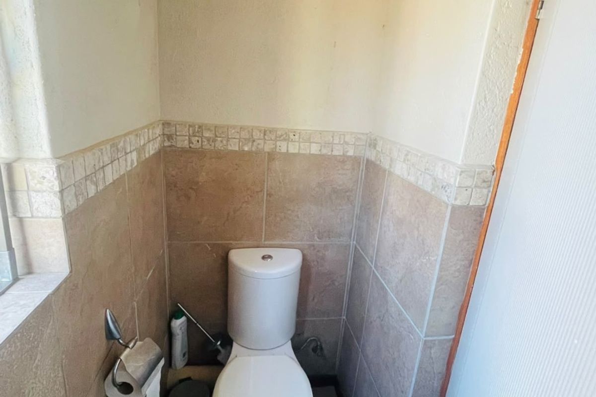 A compact guest bathroom featuring neutral ceramic wall and floor tiles with a decorative mosaic border.
