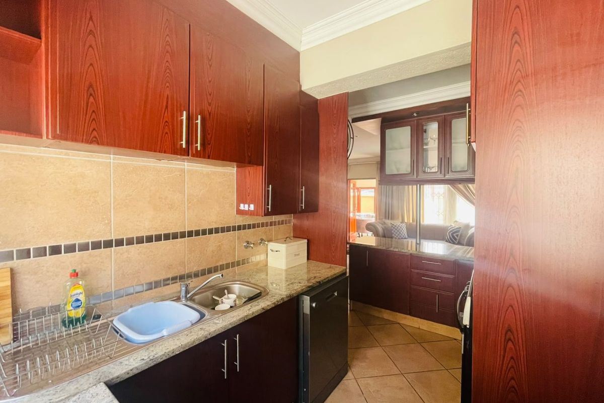 A functional kitchen featuring dark wood-look cabinetry, granite countertops, tiled backsplash, and integrated dishwasher, with an open flow into the adjacent living area.