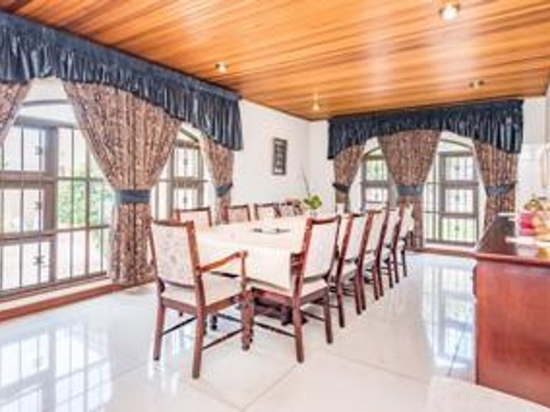 Spacious dining room featuring a warm timber-clad ceiling, large windows with security bars, and polished tiled flooring, providing a bright and functional entertaining space.
