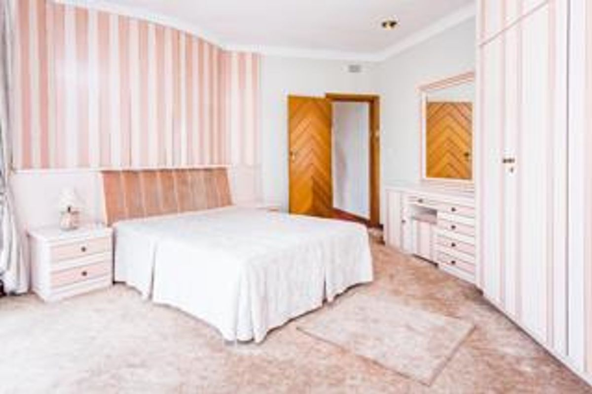 A spacious bedroom featuring built-in wardrobes, a matching vanity unit, and classic coving, offering a functional layout with dated interior finishes.