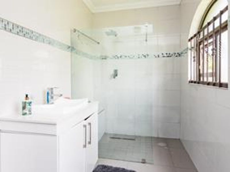 A clean, modern bathroom featuring a white vanity, basin, and a spacious walk-in shower with a glass screen and tiled finishes.