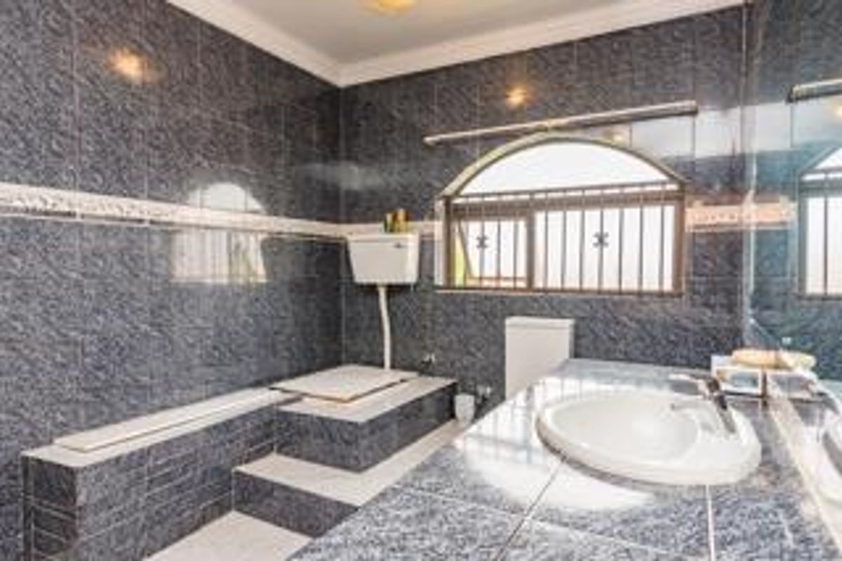 A dated bathroom featuring dark patterned wall tiles, a raised bathtub platform, a high-level cistern toilet, and a built-in vanity with a drop-in sink.