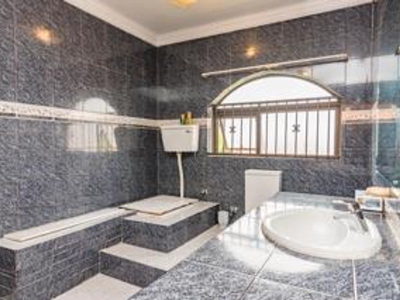 A dated bathroom featuring dark patterned wall tiles, a raised bathtub platform, a high-level cistern toilet, and a built-in vanity with a drop-in sink.
