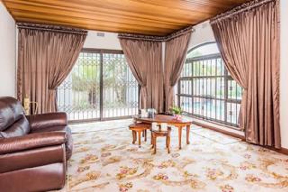 A living room featuring a timber ceiling, large windows, and sliding glass doors with security gates, offering views of the outdoor area.