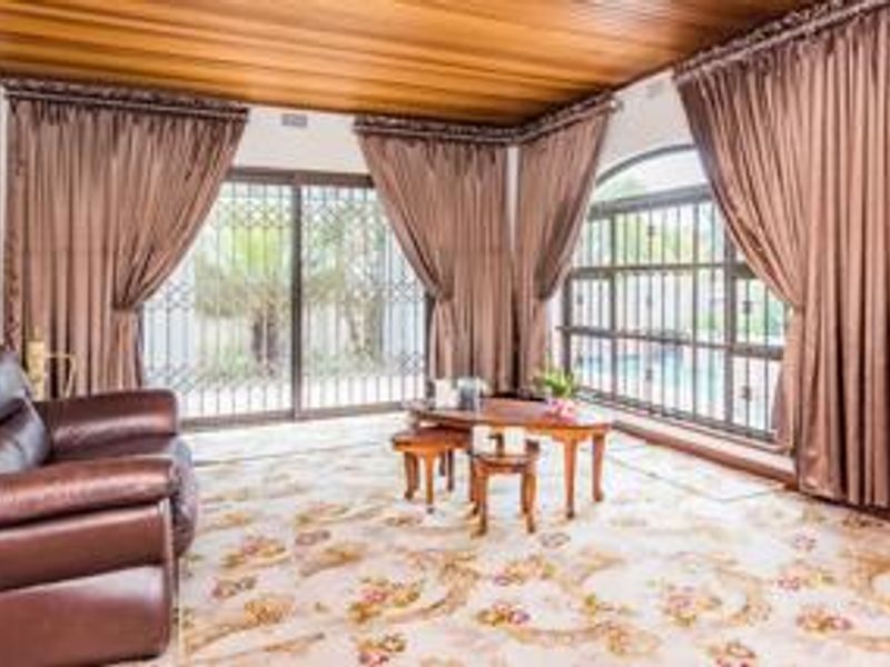 A living room featuring a timber ceiling, large windows, and sliding glass doors with security gates, offering views of the outdoor area.