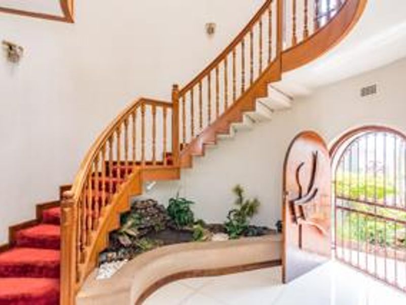 Grand entrance hall featuring a curved wooden staircase, built-in indoor planter, and an arched security gate leading to the exterior.