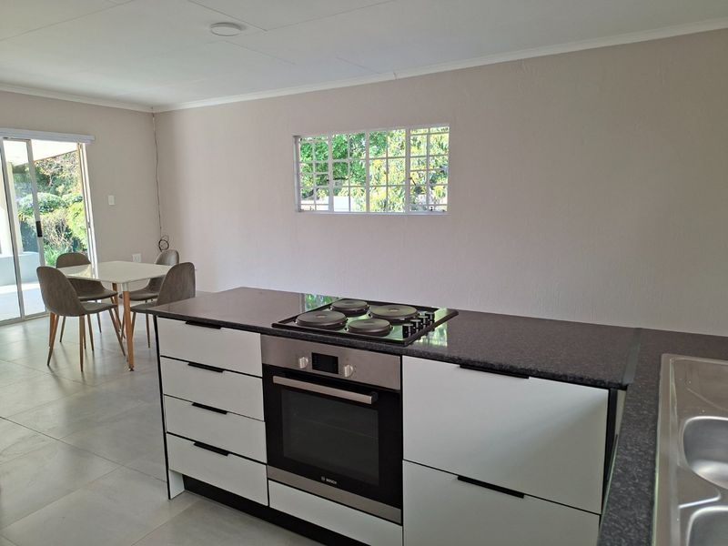 Modern open-plan kitchen featuring sleek white cabinetry, dark countertops, built-in oven and hob, with seamless flow to the dining area and outdoor access.