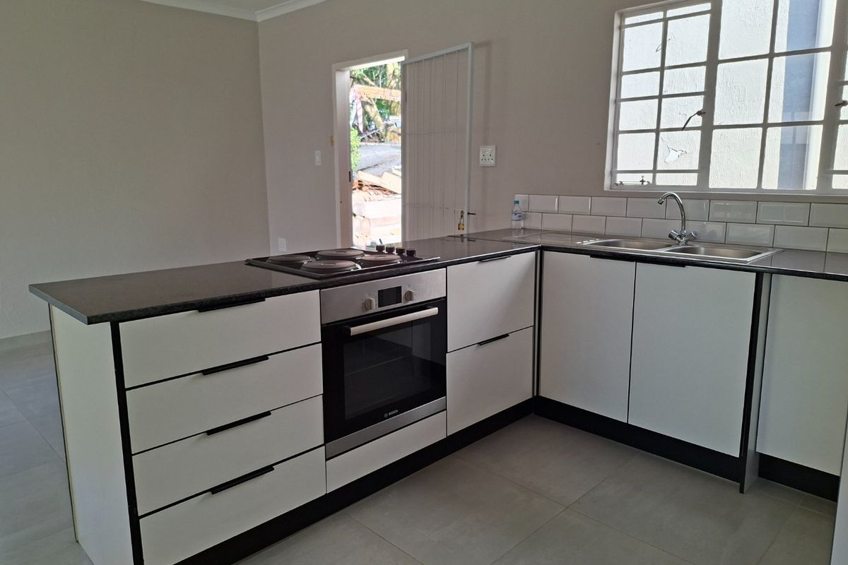 Modern kitchen featuring white cabinetry, dark stone countertops, built-in oven, electric hob, and a double sink with a tiled backsplash.