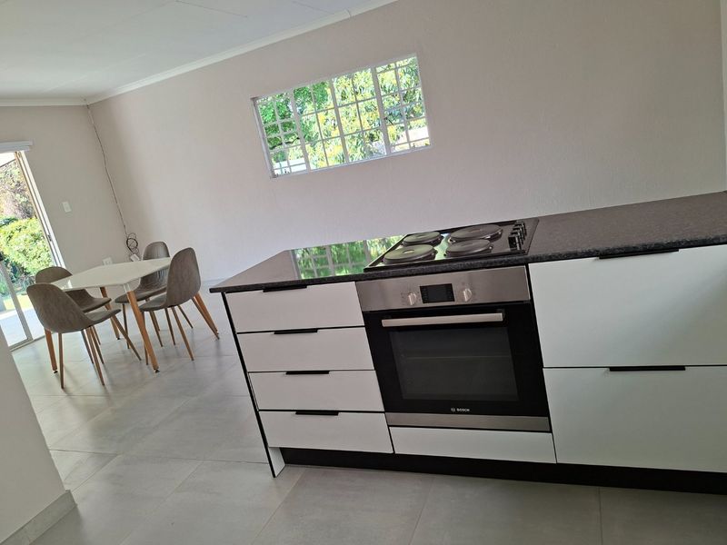Modern open-plan kitchen and dining area featuring a central island with built-in oven and hob, sleek cabinetry, and large format floor tiles.