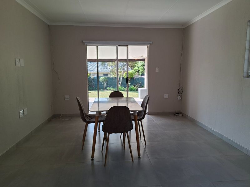 A neutrally painted living area featuring large format floor tiles and a sliding glass door providing direct access to the rear garden.