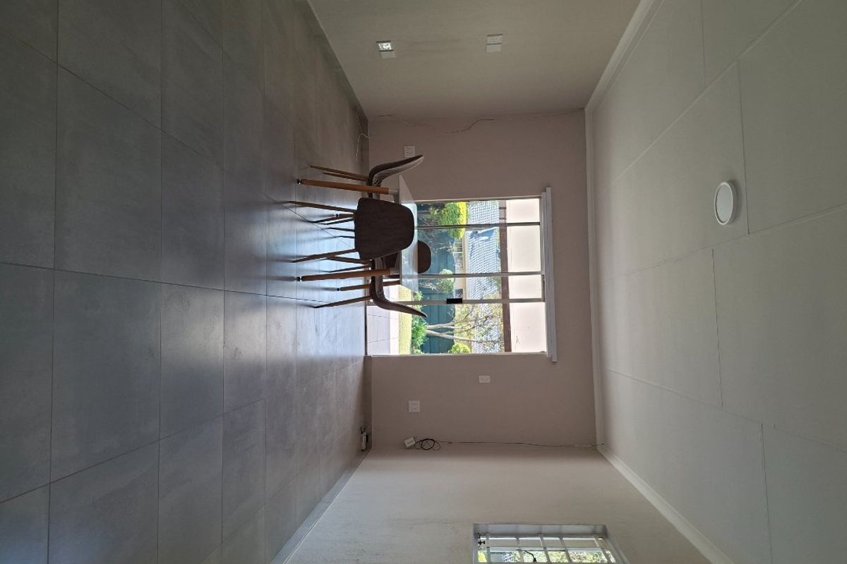 A spacious, empty living area featuring large format floor tiles, a sliding glass door to the exterior, and a window with security bars.