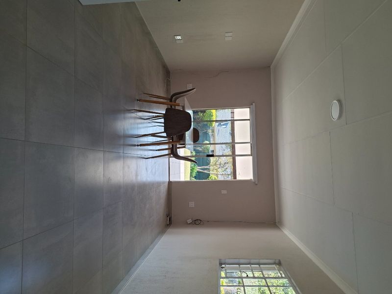 A spacious, empty living area featuring large format floor tiles, a sliding glass door to the exterior, and a window with security bars.