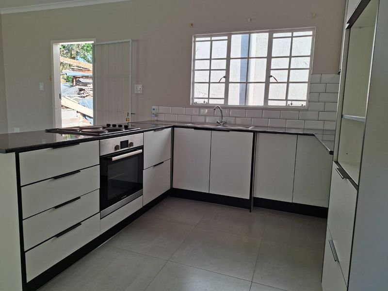 A clean, modern kitchen featuring white cabinetry, dark countertops, a built-in oven and hob, and a subway tile backsplash with tiled flooring.