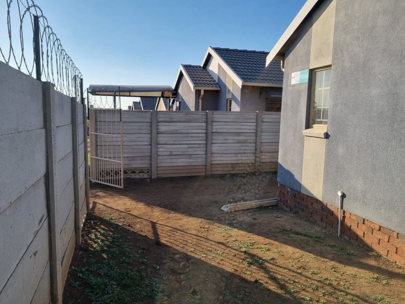 Rear exterior view of the property featuring a precast concrete boundary wall with razor wire security and an open yard area.