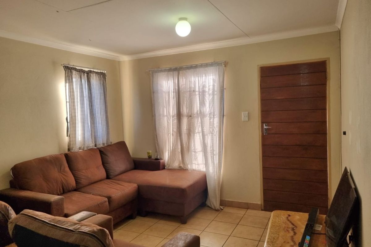 A living room featuring tiled flooring, a wooden door, and neutral wall finishes, currently showing signs of wear and maintenance requirements.