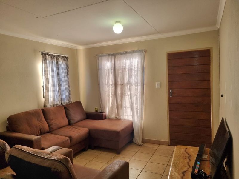A living room featuring tiled flooring, a wooden door, and neutral wall finishes, currently showing signs of wear and maintenance requirements.