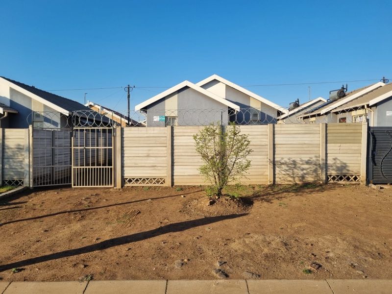 A rear yard area featuring a precast concrete boundary wall topped with razor wire and secure metal gates.