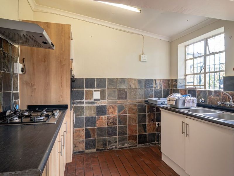 A functional kitchen featuring a gas hob, extractor fan, double sink, and slate tile splashbacks with built-in cabinetry and terracotta flooring.