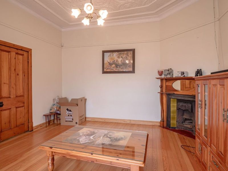 A living room featuring original timber flooring, a decorative fireplace with a timber mantel, ornate ceiling detailing, and a classic timber door.