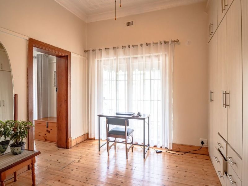 A well-lit bedroom featuring polished timber flooring, extensive built-in cabinetry, and classic architectural details including high ceilings with decorative cornicing.